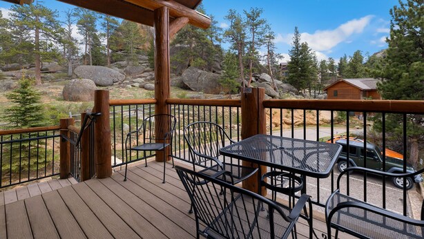 A wooden deck with metal chairs and tables, overlooking a rocky landscape with trees and a cabin. - Stylish Mountain Retreat • Near RMNP & Downtown (Estes Park)