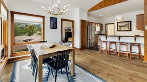 A spacious kitchen with wooden cabinets, a stainless steel refrigerator, and a dining area with a wooden table and chairs. - Stylish Mountain Retreat • Near RMNP & Downtown (Estes Park)