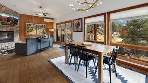 A spacious living room with a stone fireplace, a large dining table, and a view of a mountainous landscape through large windows. - Stylish Mountain Retreat • Near RMNP & Downtown (Estes Park)