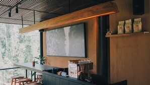 Un espace bar avec des tabourets en bois, un appareil à café et une étagère où sont rangés des sacs.