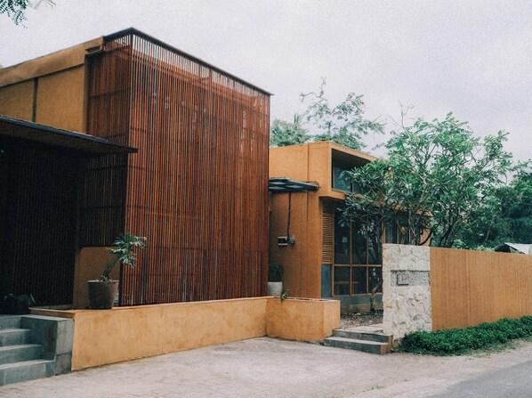 A modern building with a vertical wooden facade, a stone wall, and a concrete entrance. - Loji Nyanyi Suite & Brew (Cemagi)
