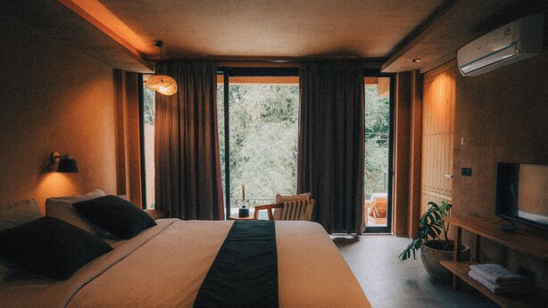 Une chambre d’hôtel avec un grand lit, une télévision, une petite table avec des chaises et une vue sur la verdure par la fenêtre.