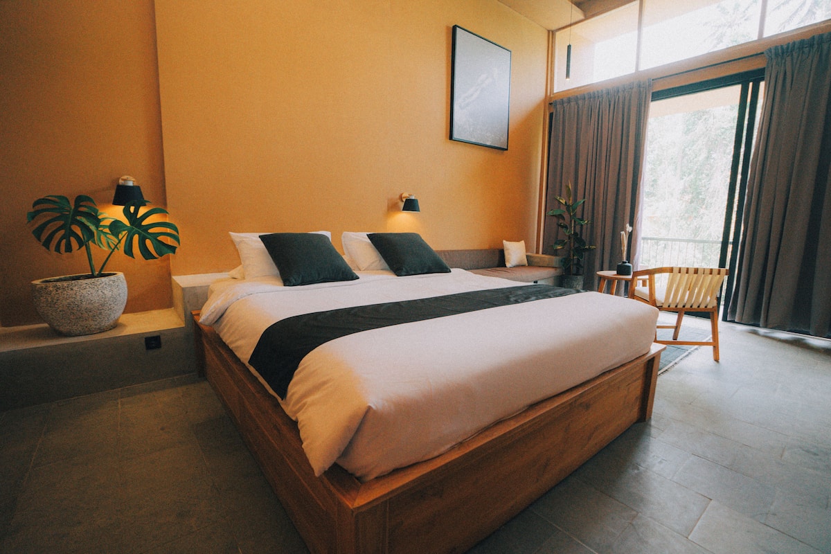 A neatly arranged bedroom with a large bed, bedside lamps, a chair, and a window with curtains.