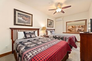Two double beds with matching headboards and footboards, a flat-screen TV, and a wooden nightstand with a lamp.