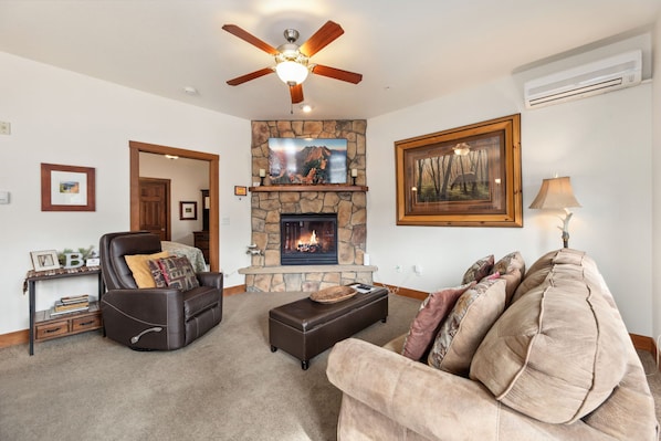 Cozy living room with a fireplace, comfortable seating, and a ceiling fan.