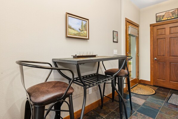 A small dining area with a table and two chairs, a door, and a wall-mounted picture.