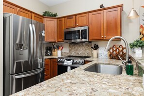 A kitchen with stainless steel appliances, wooden cabinets, granite countertops, and a stainless steel sink.