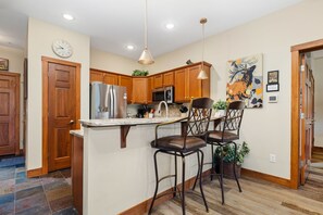 A modern kitchen with wooden cabinets, stainless steel appliances, and a bar area with stools.