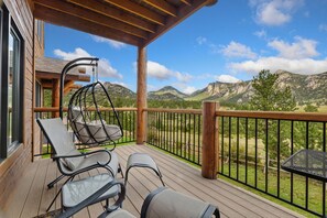 A wooden deck with outdoor furniture, including chairs and a hanging chair, overlooking a mountainous landscape.