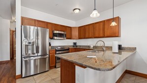 Eine moderne Küche mit Edelstahlgeräten, Holzschränken, Granit Arbeitsplatten und Pendelleuchten.