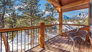 A wooden deck with a view of snow-covered mountains and pine trees.