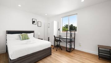 Quarto com cama, escrivaninha, cadeira e vista para o exterior.