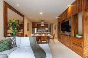 Relax in this inviting space with a sofa, TV, and potted plant, surrounded by a dining area and kitchen.