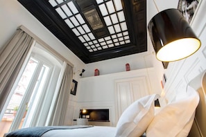 Une chambre à coucher avec un lit, un luminaire au plafond, une télévision et une fenêtre avec des rideaux.