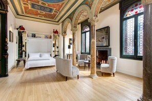 Un espacioso dormitorio con una cama grande, dos sillones, una chimenea y un techo decorativo.