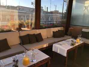 A cozy outdoor seating area with a sofa and tables set for dining, overlooking a cityscape with buildings and construction cranes. - Roof Suite Rome Suitable for 6 Persons (Rome)