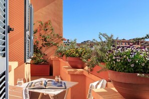 Terraza en la azotea con mesa y sillas, plantas en macetas y vistas a edificios.