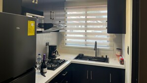 A modern kitchen with dark cabinets, a built-in microwave, a gas stove, and a window with blinds. - Fully furnished two-bedroom apartment (Cuenca)