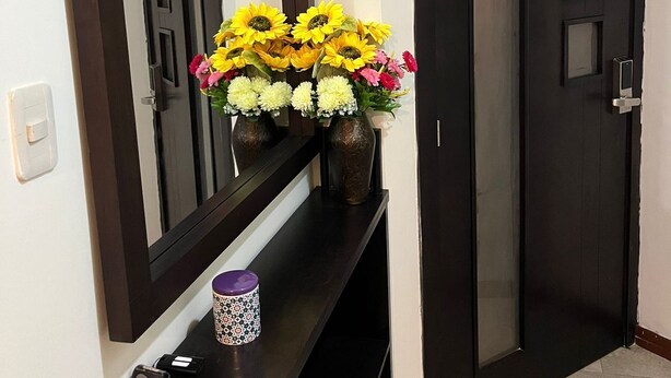 A hallway with a dark wooden door, a large mirror, and a console table with a vase of flowers and a decorative mug. - Fully furnished two-bedroom apartment (Cuenca)