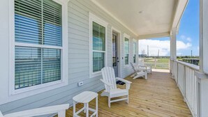 Un porche cubierto con barandas blancas, una terraza de madera y dos sillas Adirondack.