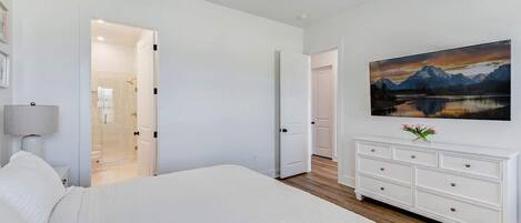 A bedroom with a bed, a dresser, a painting, and a ceiling fan.