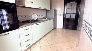 Una cuina amb armaris blancs, fogó a gas, nevera i un rellotge a la paret.
