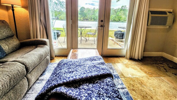 Une pièce avec un canapé, une couverture et une vue sur un patio aménagé avec du mobilier d’extérieur et un barbecue.