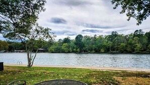 Un espace extérieur aménagé au bord du lac, avec une table et des chaises en métal, entouré d’arbres et offrant une vue sur le lac.