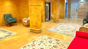 A lobby with a green armchair, a white armchair, and a red sofa. There are two large pillars and a patterned rug on the floor. - Mirage Pyramids View  (Giza)