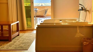 A hotel room with a bed, a bathtub, a window with a view of mountains, and a balcony with chairs. - Mirage Pyramids View  (Giza)