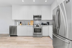 A modern kitchen with white cabinets, stainless steel appliances, and a wooden floor. - Charming LA Retreat (Los Angeles)