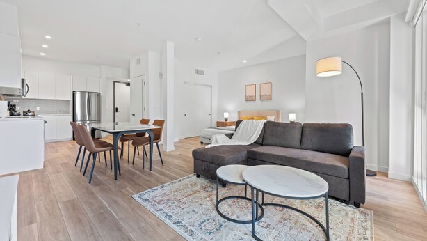 Un appartement moderne comprenant un coin repas, un salon avec un canapé et une table basse, et une cuisine équipée d’un réfrigérateur.