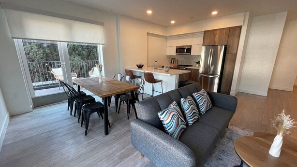 A modern kitchen with a central island, a dining area with a wooden table and chairs, and a grey sofa with patterned cushions. -  Modern Retreat in Koreatown (Los Angeles)