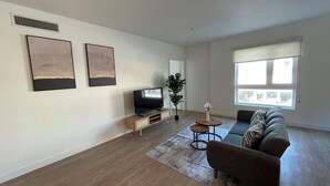 A modern living room with a flat-screen TV, a sofa, a coffee table, and artwork on the wall. -  Modern Retreat in Koreatown (Los Angeles)