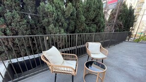 Two wicker chairs with cushions on a balcony with a metal railing, overlooking a dense row of trees. -  Modern Retreat in Koreatown (Los Angeles)