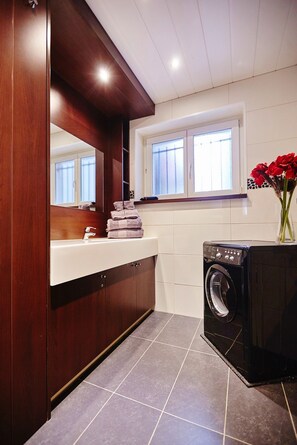 Une salle de bain moderne avec un meuble-lavabo en bois, un lave-linge encastré et une fenêtre en verre dépoli.