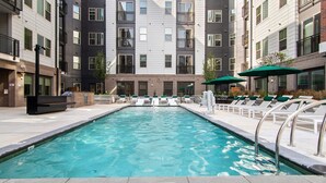 A swimming pool with lounge chairs and umbrellas, surrounded by multi-story buildings with balconies. - Landing Apartments Durham (Durham)