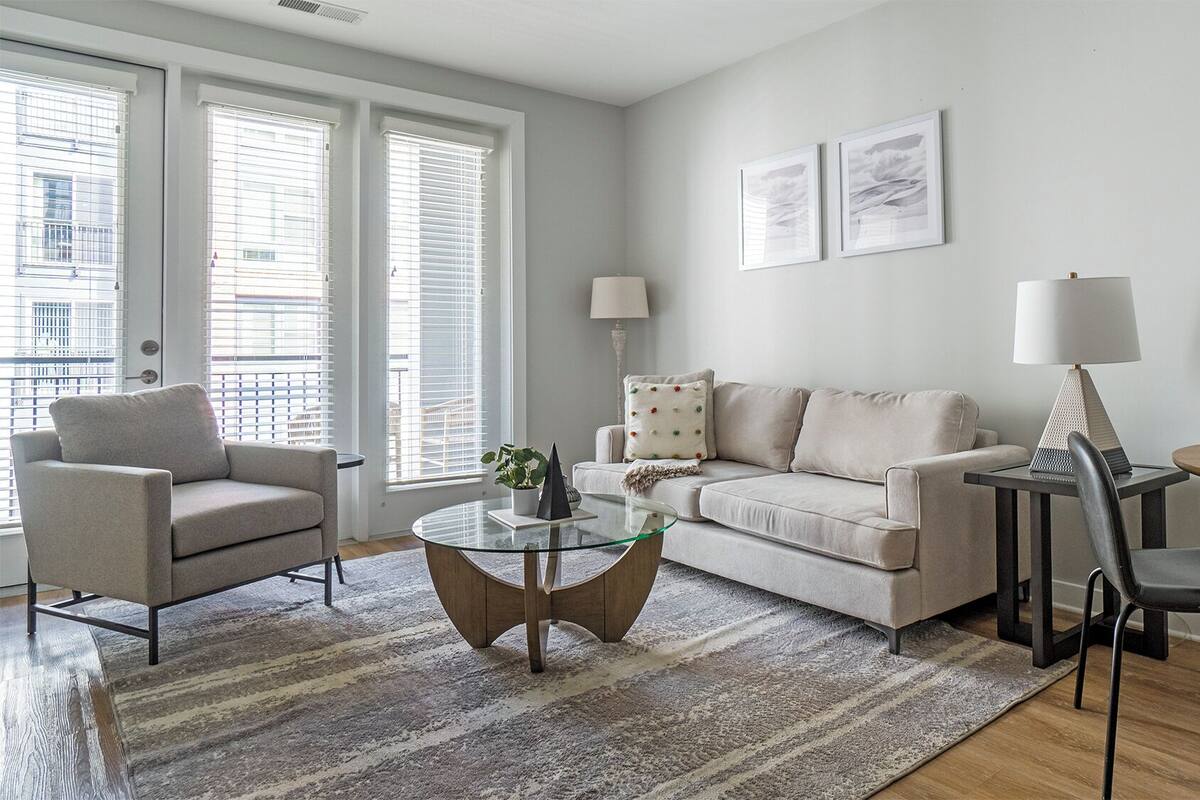 A modern living room with a sofa, armchair, glass coffee table, and a round wooden table with chairs.