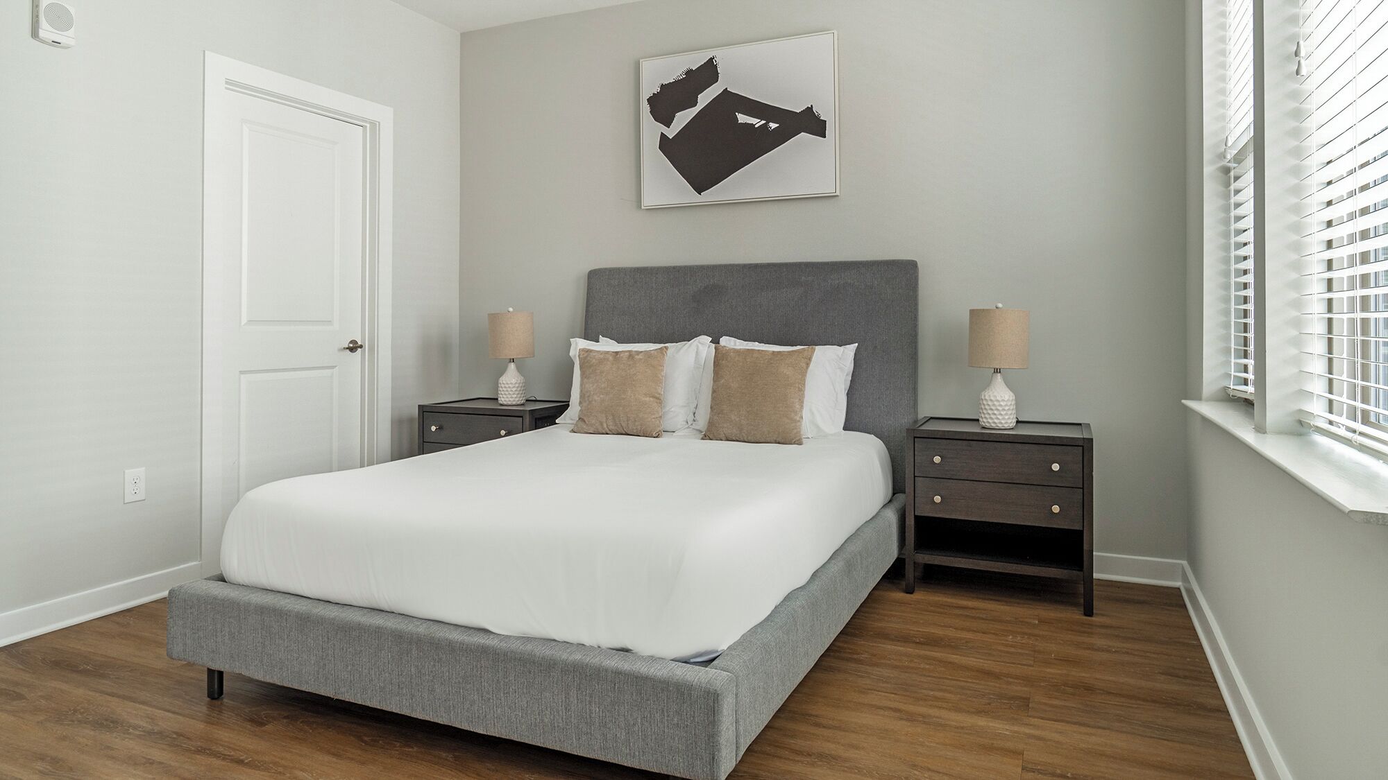 Un dormitorio con una cama grande, dos mesitas de noche, un cabecero y una obra de arte en la pared.