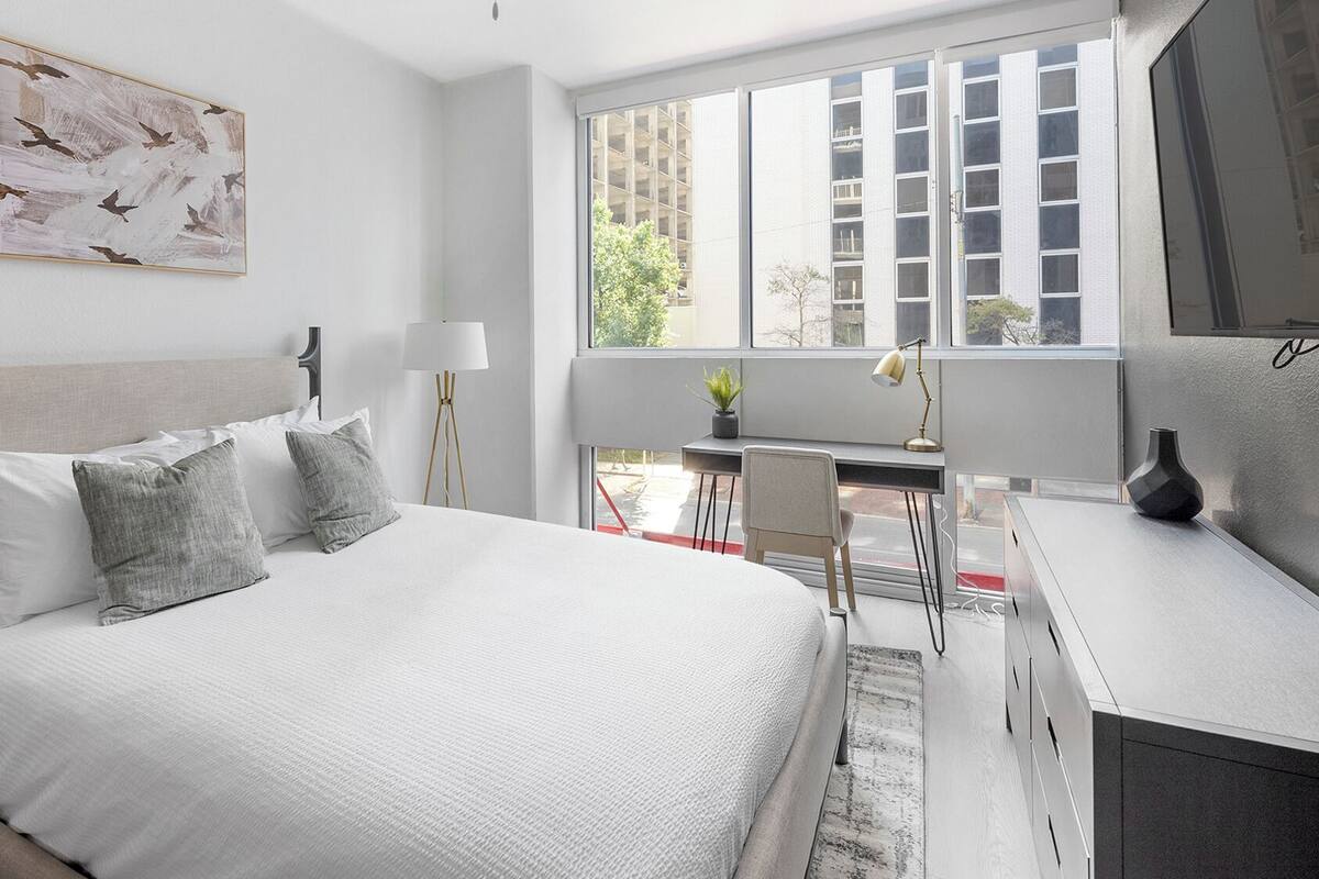 Un dormitorio moderno con una cama, mesitas de noche, un escritorio y un ventanal grande.