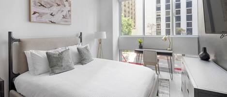 Ein modernes Schlafzimmer mit Bett, Nachttischen, einem Schreibtisch und einem großen Fenster.