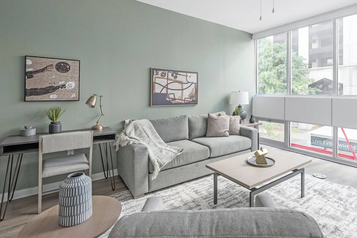 Una sala de estar moderna con un sofá gris, una mesa de centro y un ventanal con vistas al exterior.