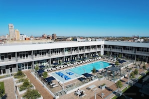 A rooftop pool area with lounge chairs and umbrellas, surrounded by a modern building with multiple floors and large windows. - Landing Midtown (Birmingham)