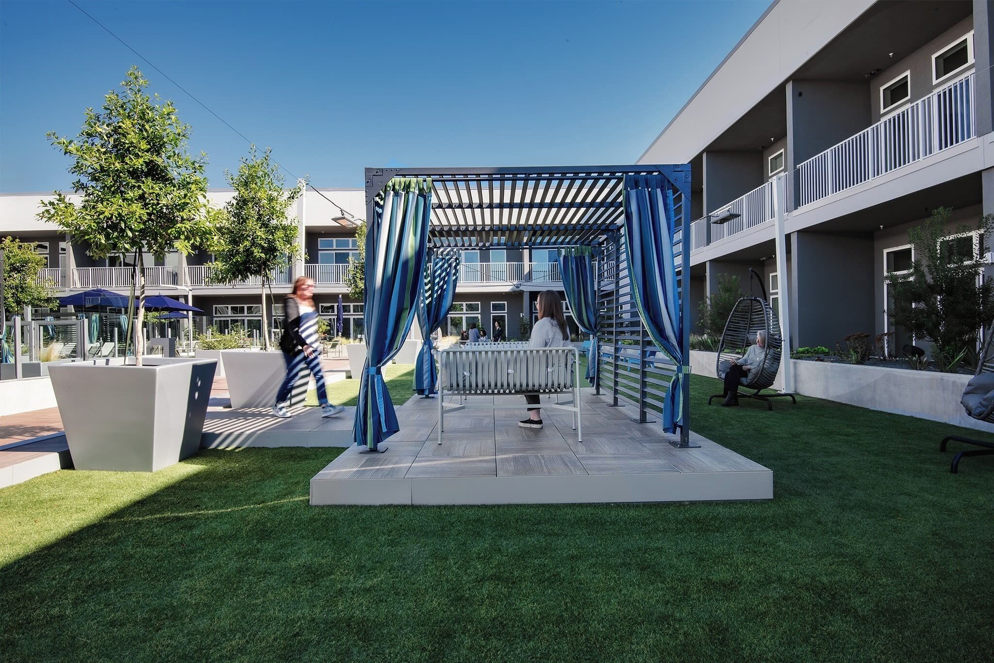A modern outdoor seating area with a pergola, benches, and a grassy lawn.