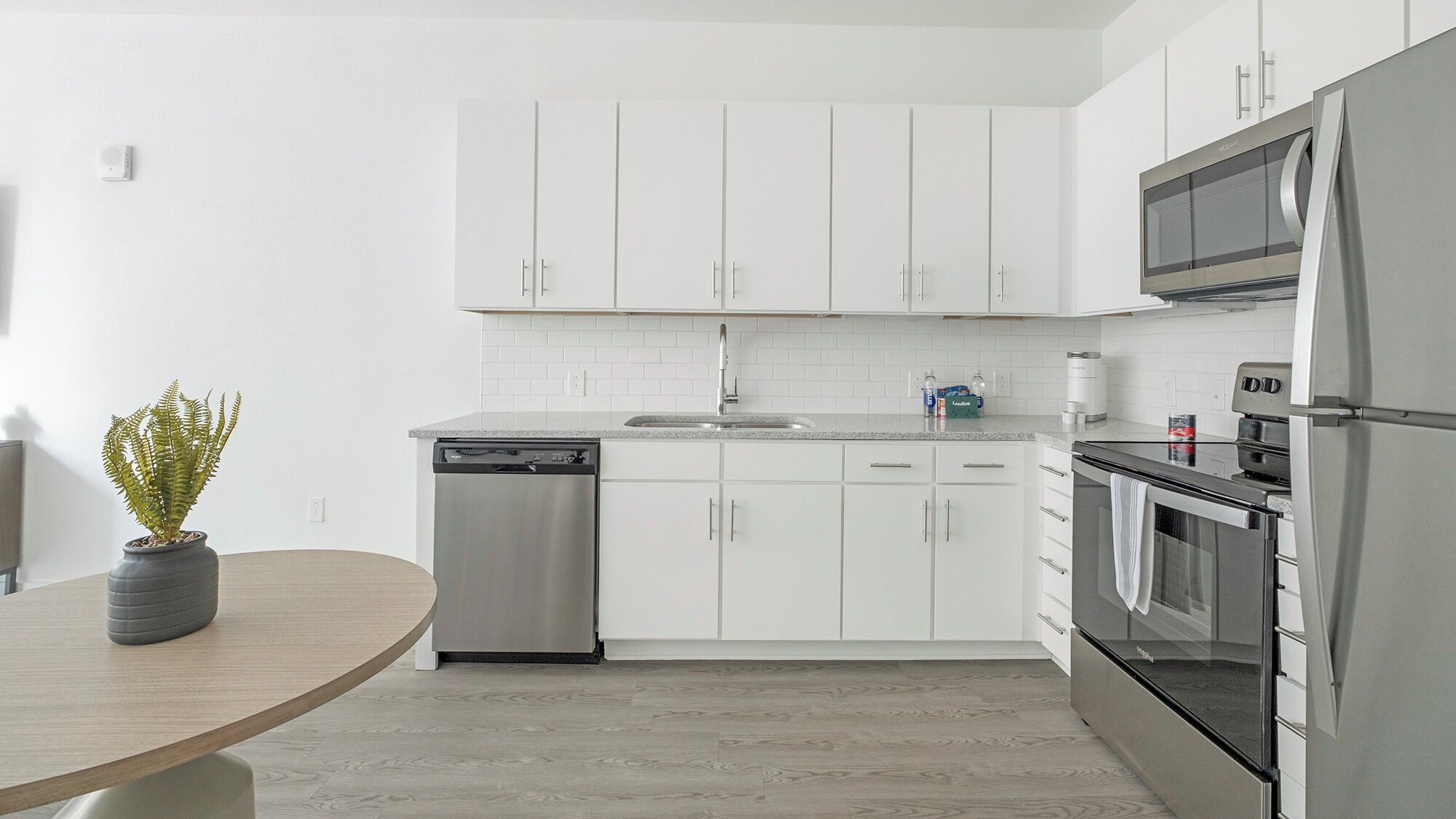 A modern kitchen with white cabinets, stainless steel appliances, and a wooden dining table.