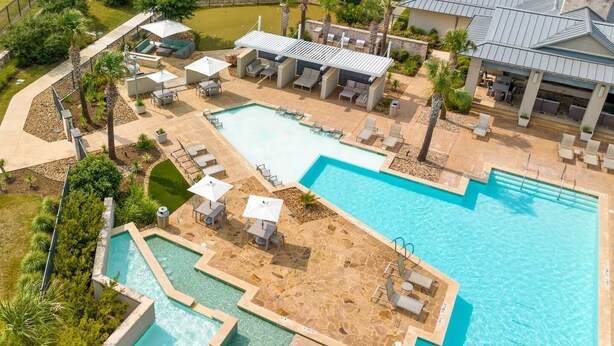 A large outdoor swimming pool with multiple sections and lounge areas, surrounded by palm trees and a covered seating area.