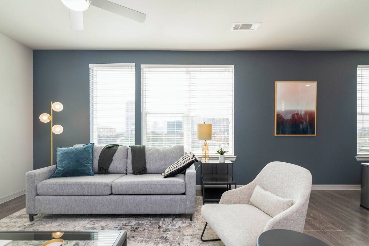 Ein modernes Wohnzimmer mit einem grauen Sofa, einem weißen Sessel, einer Stehlampe und einem Stadtbild an der Wand.