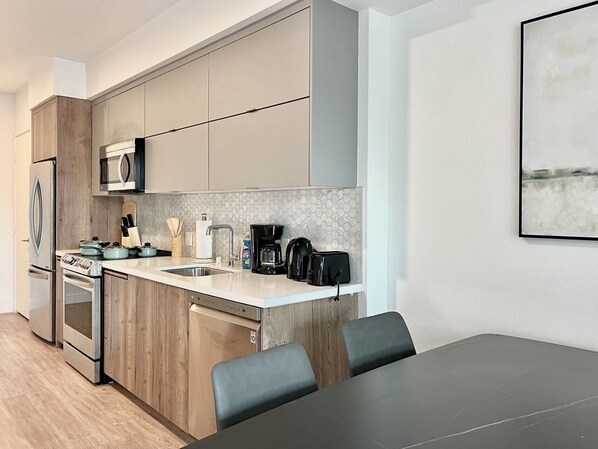A modern kitchen with wooden cabinets, stainless steel appliances, a marble backsplash, and a dining area with a black table and chairs. - Stylish LA Studio Prime Location (Los Angeles)
