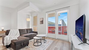 A modern living room with a sofa, two small tables, a TV, and a view of the city through large windows. - Stylish LA Studio Prime Location (Los Angeles)