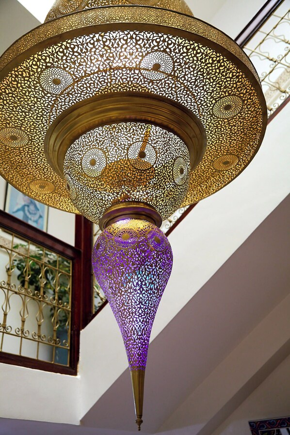A hanging lamp with intricate golden lattice design and a purple base. - Riad Amber Zahra (Marrakech)